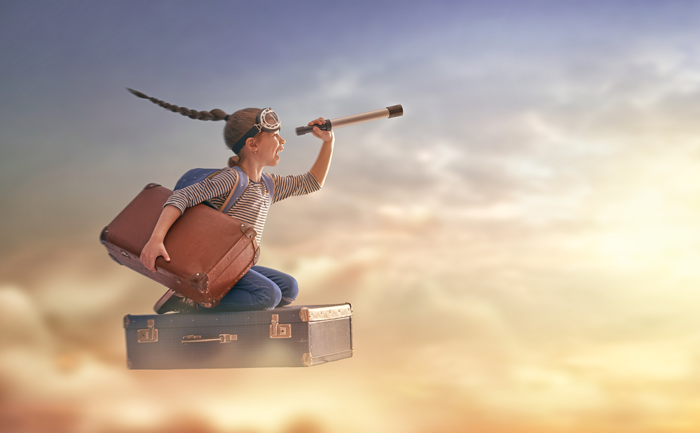 Child flying on a suitcase against the backdrop of sunset.